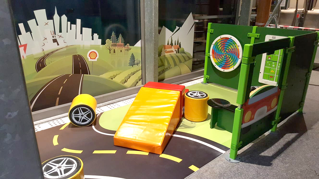 Coin de jeu pour enfants dans une station-service Shell en France, avec divers modules de jeu et des jeux muraux.